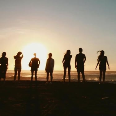 group of people standing on a beach at sunset