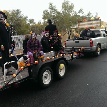 People with white facepaint sitting in trailer being pulled by truck at Halloween Parade