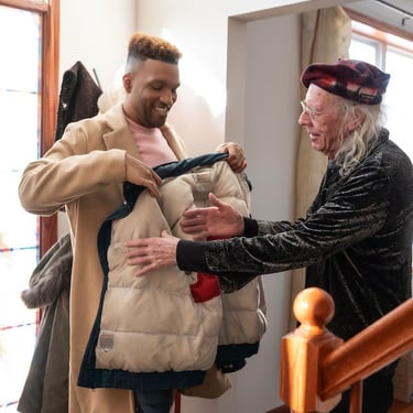 A male caregiver helps an elderly man put on his coat