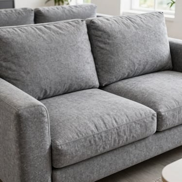 Bright clean commercial photography of a comfortable grey fabric L-shaped sofa with clean cushions, bright showroom setting, natural daylight, crisp details, 35mm lens.