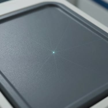 Macro photograph of a medical scanner's matte dark grey surface and a subtle laser alignment light, clean geometric lines, clinical precision, soft shadows.