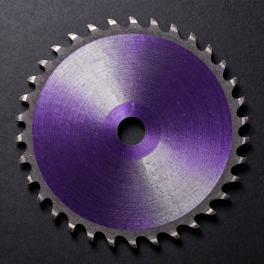 Extreme macro overhead view of a 12 inch TROOX circular saw blade, dense 96-tooth carbide geometry in sharp focus, deep violet metallic body on matte black studio surface, controlled directional strobe light raking across tooth tips