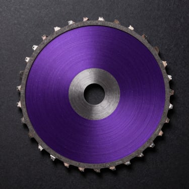 Extreme macro overhead view of a 7-1/4 inch TROOX circular saw blade, carbide teeth in sharp focus against matte black background, deep violet metallic body surface, studio strobe lighting revealing micro-bevel tooth geometry