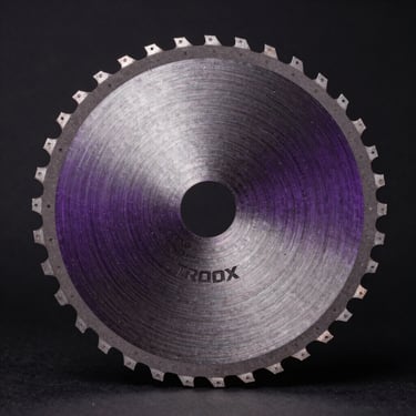 Extreme macro overhead view of a 14 inch TROOX circular saw blade, 120-tooth carbide precision edge array in sharp studio focus, metallic violet body with industrial finish, controlled strobe lighting on matte black backdrop