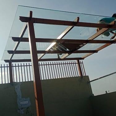 Minimalist glass pergola with a dark metal frame installed on a modern residential terrace.