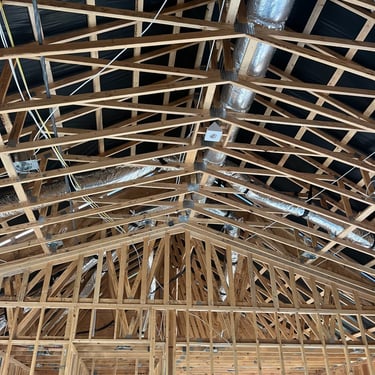 New home construction showing exposed roof trusses, ductwork, and a rough-in HVAC installation for future heating and cooling