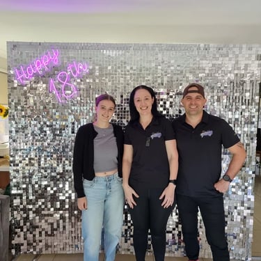 Laura and SweetAz crew in front of the silver shimmer wall and happy 18th neon after relocating.