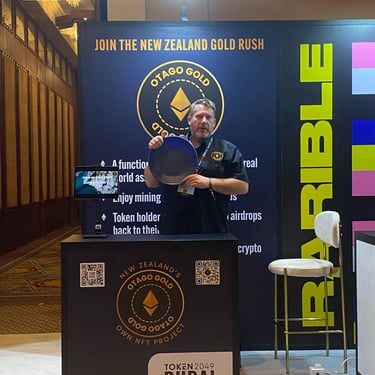A photograph of Chris Prichard, at the Token2049 Dubai event, holding up a gold pan.