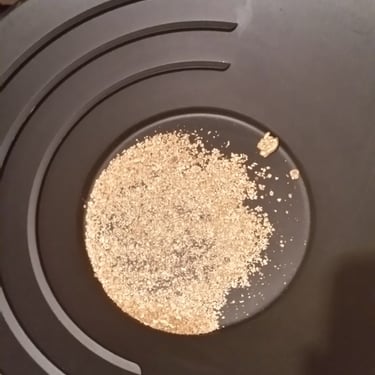 A photo of a black gold pan, with a large amount of various sizes of gold. New Zealand 