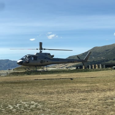 A photograph of a helicopter taking off with scenery of the nearby hills and mountains of Central Otago, New Zealand