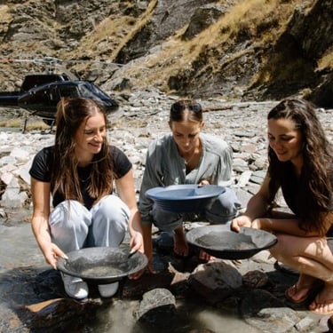 Gold Panning in Central Otago at one of Otago Gold's Claims, three young women panning and a helicopter in the background