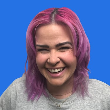 a smiling person with pink hair and a grey t-shirt