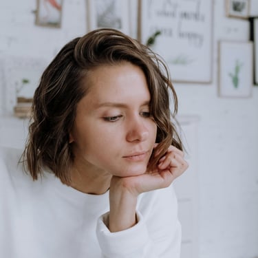 A woman with a classic bob haircut looks thoughtful as she rests her chin on her hand. Her hair, cut just above the shoulders