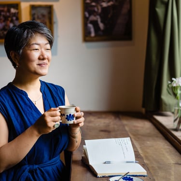 femme trentenaire asiatique qui tient une tasse devant une fenêtre ensoleillé