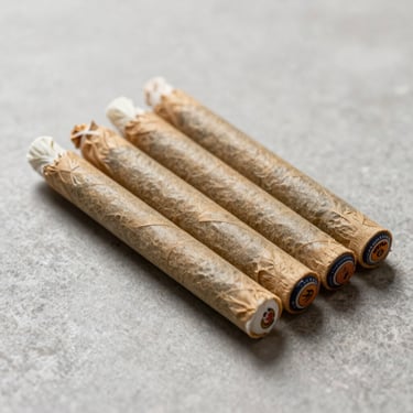 Three perfectly rolled, uniform cannabis pre-rolls with custom branded tips, arranged neatly in a parallel line on a clean stone surface.