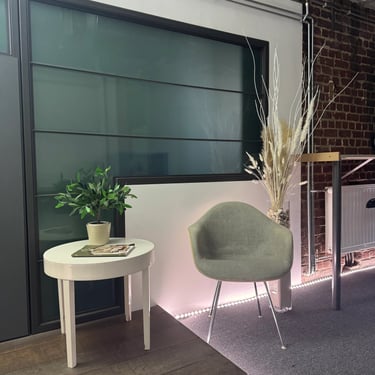 Coin détente avec fauteuil, petite table blanche avec plante, vase de pampa, vitre opaque et mur en briques.
