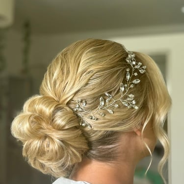 Low bridal bun with soft texture and a crystal hair accessory for an elegant wedding look