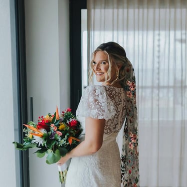 Smiling bride holding a colorful bouquet with soft waves and elegant bridal styling by Deya Ventura in Punta Cana