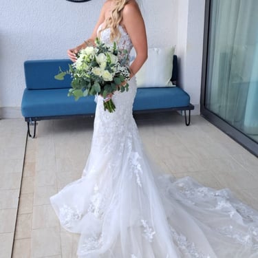 Bride in a lace wedding dress holding a white and green bouquet with soft waves and a jeweled headpiece