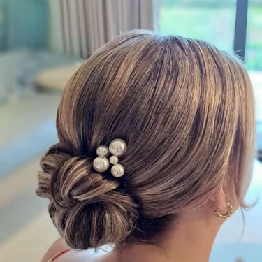 Low bridal bun with a pearl hair accessory for a simple and elegant wedding hairstyle