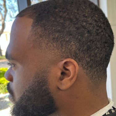 Side profile of a person with short, textured hair and a neatly trimmed beard.
