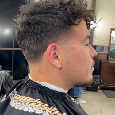 Side profile of a man with a curly top hairstyle and fade in a barbershop.