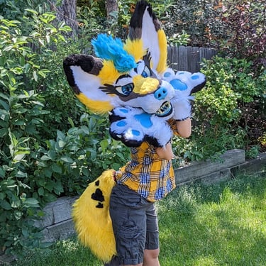 A yellow coyote fursuit featuring a full jaw set of silicone teeth and big ears as well as glow in the dark parts From Teto