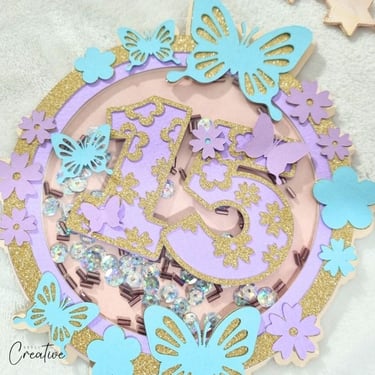 Round cake topper, shaker, in pastel purple and blue with gold accents with number 15 inside.
