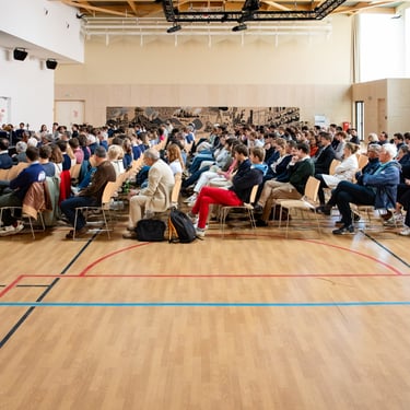 Une foule de personnes réunies et assises au milieu d'une salle de sport