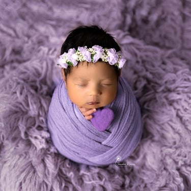 recién nacida envuelta con tocado y un corazoncito violeta