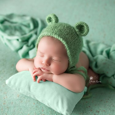 recién nacido con gorrito de orejitas sobre almohada verde