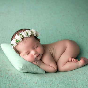 recién nacido con tocado dormida sobre almohada verde