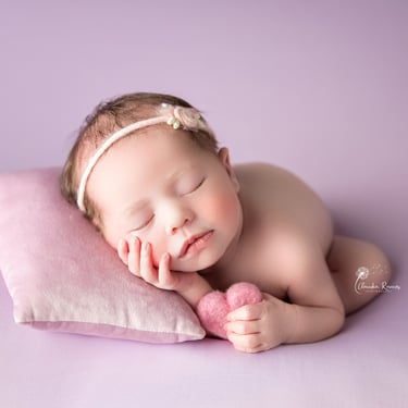 recién nacida con corazoncito en la mano sobre fondo violeta