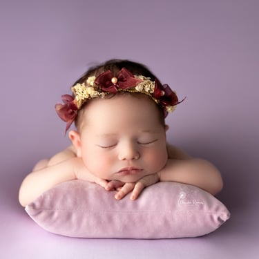 recién nacida con tocado dormida sobre almohada violeta
