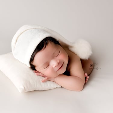recién nacida dormidita sobre almohada con gorrito blanco