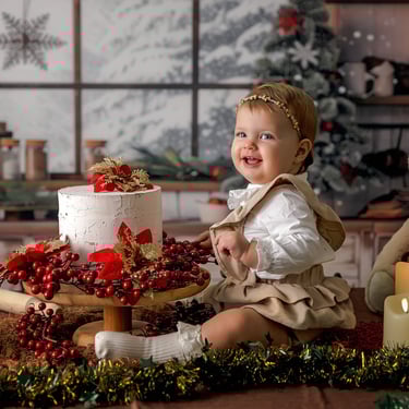 bebé en fondo navideño sentada al lado de una tarta