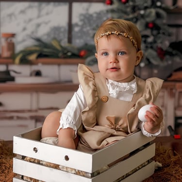 niña en una cajita con ún árbol de navidad al fondo