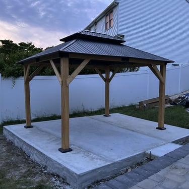 A recently-assembled wooden gazebo with a two-tiered metal roof.