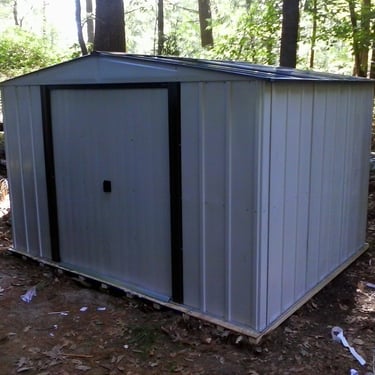 A white metal shed assembled on a plywood platform for a client's backyard.