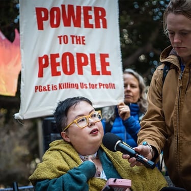 Photo of Stacey at a protest with sign that reads "power to the people PG&E is killing us for profit"