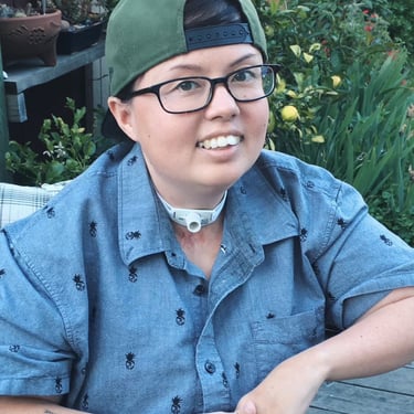 Picture of Stacey laid back, in casual clothes with a backwards hat, smiling, with arms folded together.