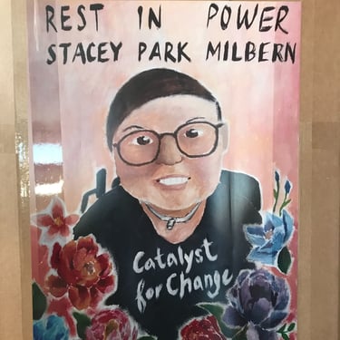 Photo of poster of Stacey which says "Rest In Power Stacey Park Milbern" with flowers and shirt with "catalyst for change"