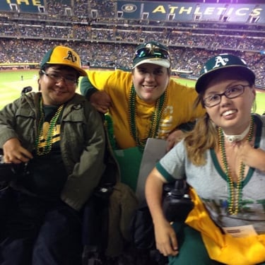 Photo of Stacey at an Oakland A's game with friends. She has mardi gras beads and Atheltics gear on at the game.