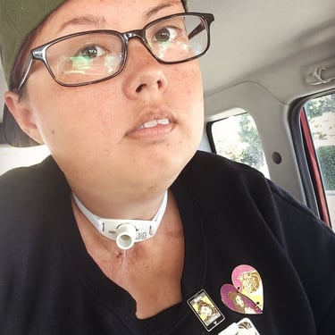 Photo of Stacey with a backwards hat and pins on her shirt riding in her car.