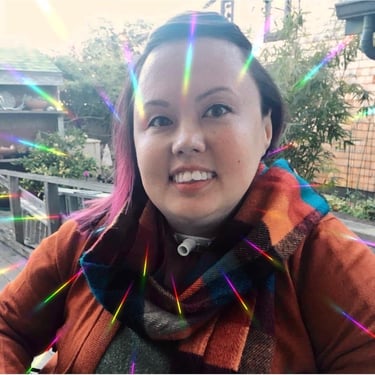 Picture of Stacey smiling, wearing fall colors, with pink hair, and an instagram filter with glare.