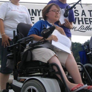Photo of Stacey speaking at a MLK event on stage into a microphone , holding a sheet of notes.