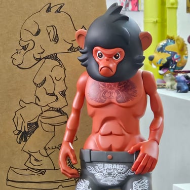 Red monkey designer toy figure with tattoos and black hair in an urban art studio setting.