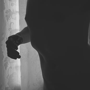 Hombre de torso y mano en contraluz frente a cortina traslúcida.