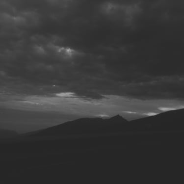 Paisaje de montañas bajo un cielo oscuro y nublado en blanco y negro.