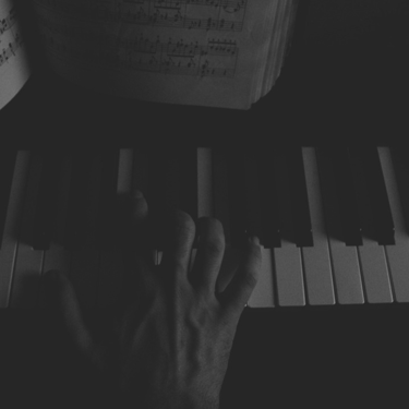 Mano tocando teclas de piano bajo luz tenue y partitura al fondo.